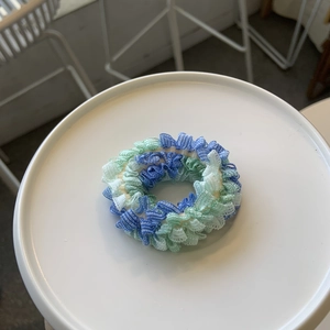 Chouchou en dentelle aux textures plissées bleues et vertes sur plateau blanc épuré