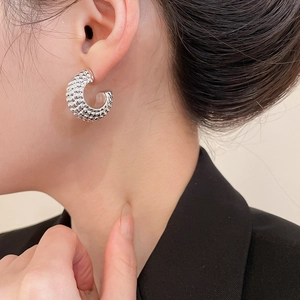 Macro side view of silver C-shaped earrings with beaded texture worn on model ear