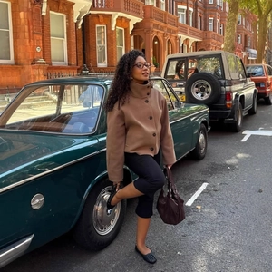 Retro brown high neck wool coat styled with black slim pants near a vintage car