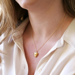 Close-up of heart-shaped gold photo locket necklace with red gemstone on a model