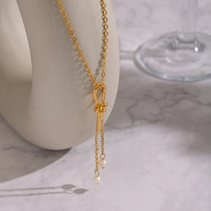 Elegant gold knot sweater chain necklace with freshwater pearl tassels on marble background