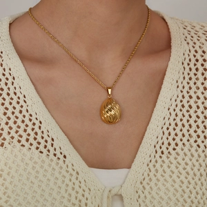 Golden teardrop pendant necklace with spiral texture on rope chain worn by a model