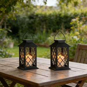 Close-up of two vintage black outdoor lanterns with warm LED candles on a wooden table