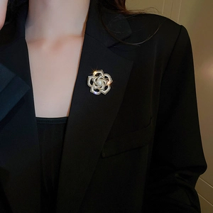 Gros plan d'une broche camélia en or avec zircons et perle sur le revers d'un costume noir