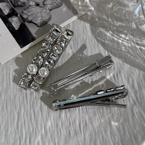 Elegant silver hair clips with shimmering crystals and white pearls on a textured background