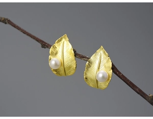 Detailed view of golden leaf-shaped earrings with white pearls on a natural wooden branch