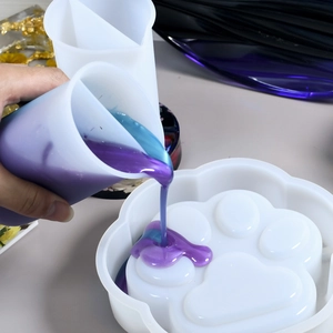 Macro shot of pouring purple resin into a cat paw silicone mold with a dual-chamber cup