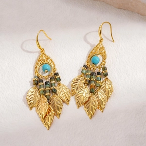 Détail de boucles d'oreilles bohèmes avec perles turquoise et pompons feuilles dorées sur tissu