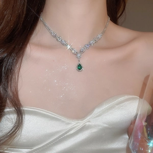 Detailed close-up of a silver necklace with a green water drop zircon pendant on neck