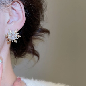 Close-up of elegant gold snowflake stud earrings with sparkling zircon on model's ear