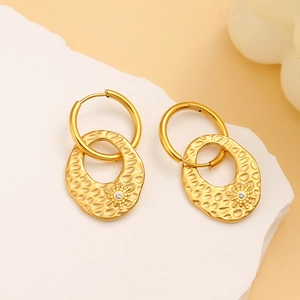 Detail of gold hammered earrings with a sparkling single diamond on a stone surface