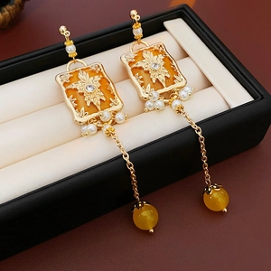 Detail of vintage gold earrings with orange enamel, pearls, and tassel chain in a box