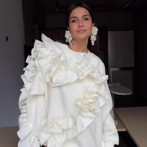 Dettaglio felpa bianca con volant, scollo a strati e orecchini a fiori color crema