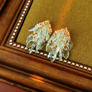 Vue détaillée de boucles d'oreilles dorées avec pierres bleu clair sur tissu vert