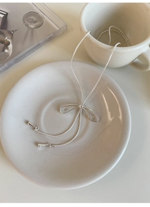 Collana con ciondolo a fiocco argento su catena a serpente in un piatto di ceramica