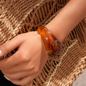 Macro detail of amber acrylic spiral cuff bracelet styled with a woven vacation bag