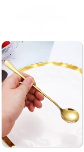 Close-up of long handle gold stainless steel mixing spoon held over table