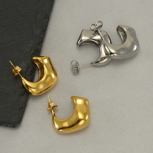 Chunky irregular C-shaped hoop earrings in gold and silver finish on textured stone