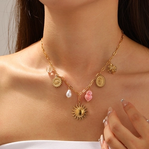 Close-up of gold chain necklace with sun, pink heart, and pearl charms on a model