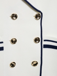 Close-up of white knit fabric with gold embossed buttons and navy blue trim detail