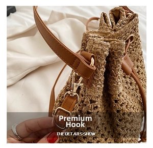 Close-up of golden metal hook and brown leather trim on woven straw bucket bag