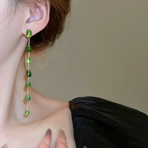 Detail of elegant gold earrings with irregular green faceted beads on metal chain