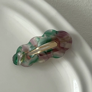 Détail d'une barrette à cheveux en acétate ondulé avec marbrures vertes et dorures