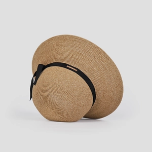 Close-up of woven straw sun hat detailing black ribbon bow and metal brand logo