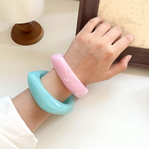 Macro view of wide thick resin bangles in light blue and pink on a soft neutral tabletop