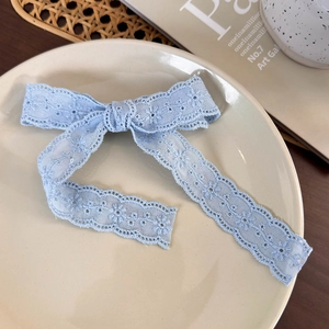 Close-up of a blue lace bow hair clip with floral embroidery on a ceramic plate