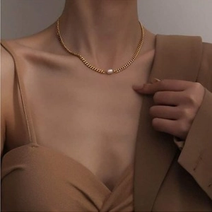 Detail view of gold pig nose chain necklace with a single white pearl on female model