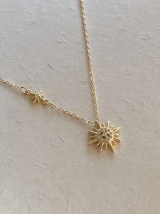 Detailed view of a gold starburst sun necklace with crystals and a small star charm