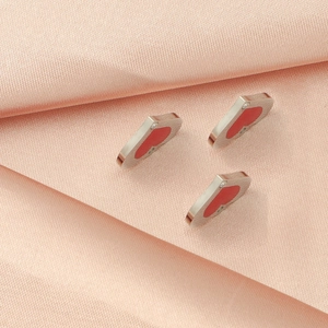 Three silver heart pendants with red inlay and crystal accent on pink silk background