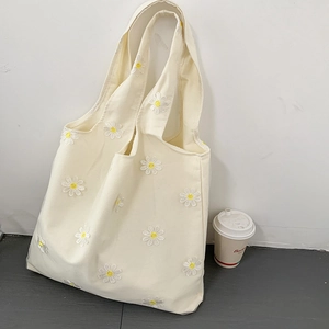 Dettaglio del ricamo di margherite bianche su borsa tote in tela color crema con tracolla