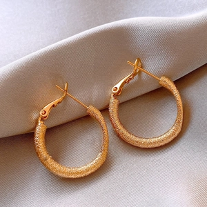 Detailed close-up of golden hoop earrings with textured stardust finish on silk fabric