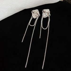Detail view of silver floral stud earrings with long metal tassel chains on black surface
