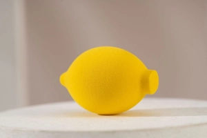 Detailed macro shot of a lemon-shaped makeup sponge with porous texture on a white stand