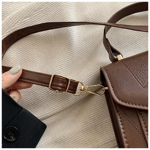 Détail du sac bandoulière en cuir marron foncé avec boucle dorée et matelassage en V