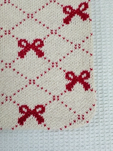 Close-up of knit tote bag showing cream fabric with red bow and diamond patterns