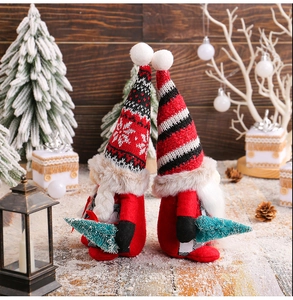 Detailed view of two Christmas gnomes with knit hats holding mini trees in snowy decor