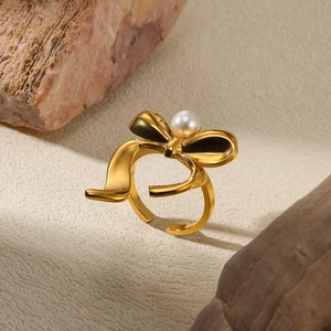 Detailed close-up of a gold bow ring with center pearl on textured stones
