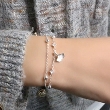 Detail shot of a double-layered silver bracelet featuring a ginkgo leaf charm and beads