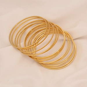 Macro view of stacked vintage gold minimalist bracelets on a soft beige fabric background