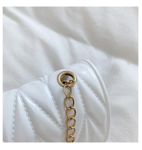Detail of white quilted crossbody bag featuring glossy texture and gold chain strap
