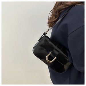 Detail of black patent leather shoulder bag featuring a U-shaped metallic buckle on strap