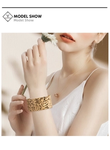 Model wearing a wide golden cuff bracelet with irregular hammered texture in soft light