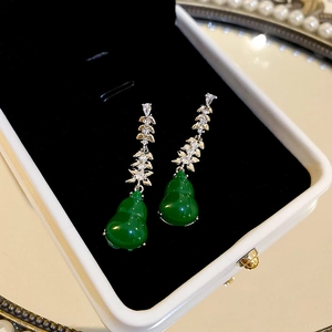 Macro shot of green gourd earrings with gold diamond-encrusted leaf hooks on black velvet