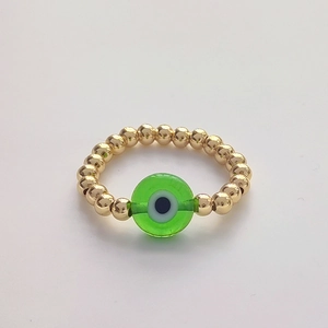 Macro detail of 18K gold-plated beaded ring with green glass evil eye charm ornament