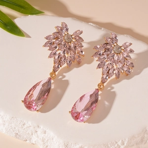 Macro shot of pink pear-cut crystal earrings with floral studs on white stone