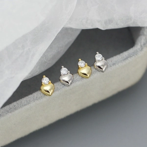 Detailed view of silver and gold heart stud earrings with round zircons on grey velvet
